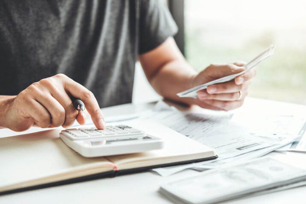 A person in a gray shirt calculates finances with a calculator, pen, and bills. The image accompanies content on negotiating severance, and suggests managing personal costs.